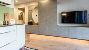 A modern kitchen with a built-in TV, wooden flooring, and a grey accent wall. - Mali Appartments Lounge (Tirolo)