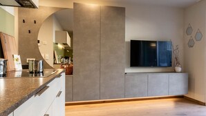 A modern kitchen with a built-in oven, a large island with a granite countertop, and a flat-screen TV mounted on the wall. - Mali Appartments Lounge (Tirolo)
