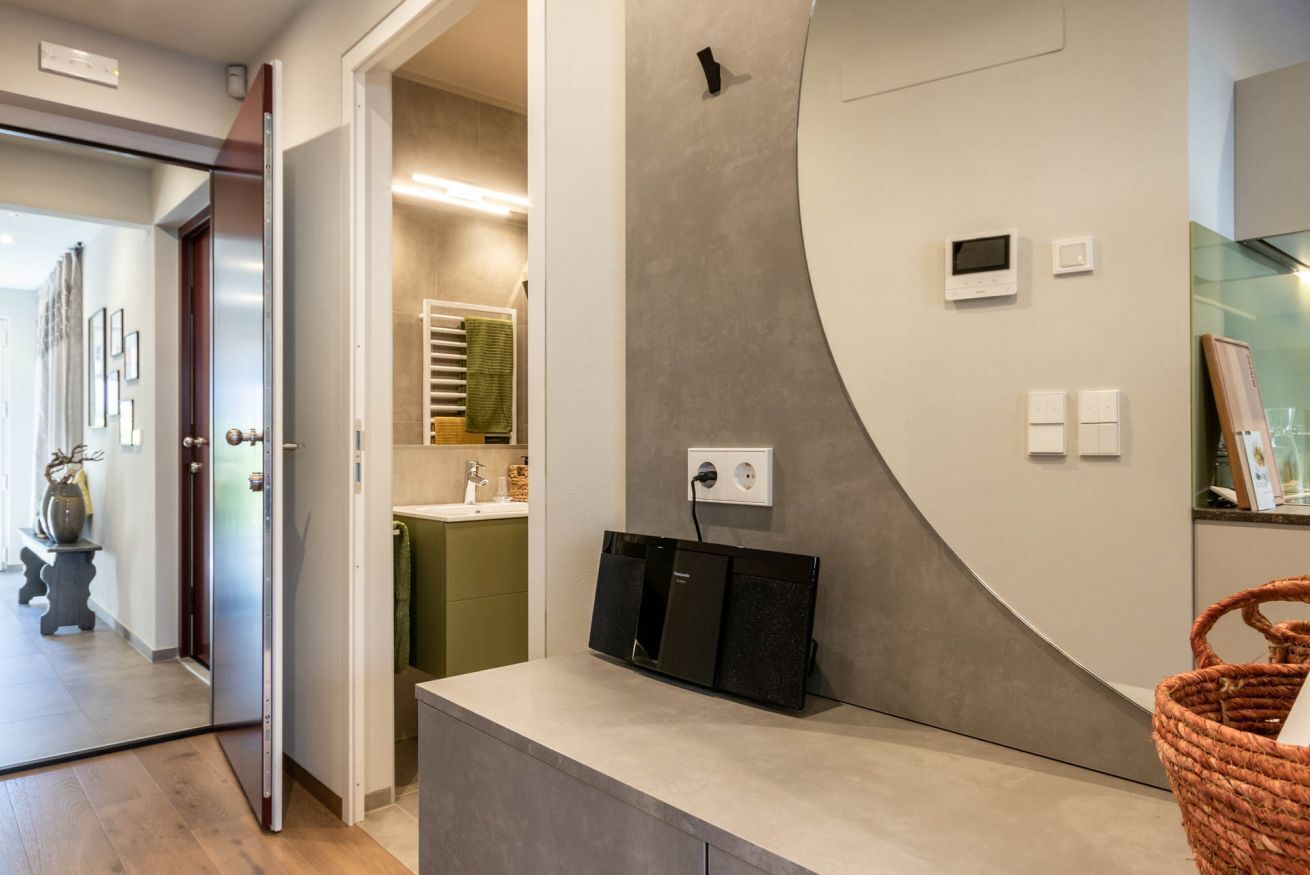 A modern bathroom with a curved wall, a sink, and a mirror. There is a towel rack and a basket on the counter.
