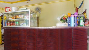 A reception area with a wooden counter, a glass display case with snacks, a fan, and a 'Reception' sign. - OYO 91766 Fortuna Hotel Syariah (Paiton)