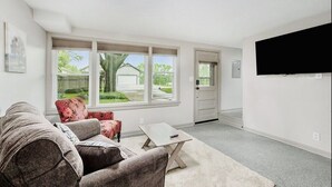 A living room with a large window, a flat-screen TV, a sofa, and a coffee table. - Recently remodeled home with bedrooms and living spaces on the ground floor (Smithville)