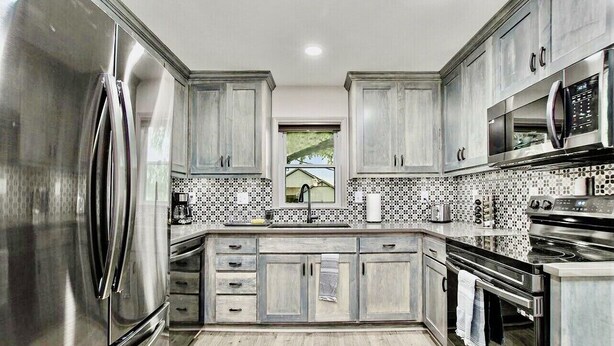 A modern kitchen with stainless steel appliances, wooden cabinets, and a patterned backsplash. - Recently remodeled home with bedrooms and living spaces on the ground floor (Smithville)