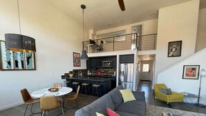 A modern living room with a grey sofa, a dining table with chairs, a kitchen area with a refrigerator and stove, and a staircase leading to an upper level. - Our Happy Place -Downtown Dazzling S Mountain View (Salida)