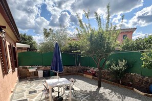 Een terras met een tafel, stoelen, een blauwe parasol en een boom.