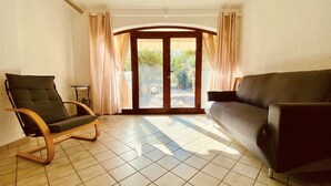 A living room with a dark green chair, a dark sofa, and a sliding glass door leading to an outdoor area. - Domo Magenta, Three-room apartment with garden near the center of San Teodoro (San Teodoro)
