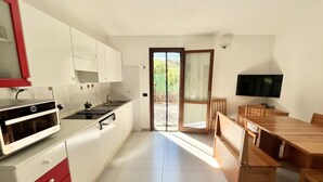 A kitchen with white cabinets, a red oven, and a dining area with wooden furniture. - Domo Magenta, Three-room apartment with garden near the center of San Teodoro (San Teodoro)