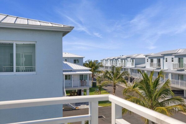 Une rangée de bâtiments blancs d’un motel, dotés de balcons, sous un ciel dégagé, avec des palmiers.