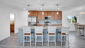 A modern kitchen with a central island, wooden cabinets, stainless steel appliances, and pendant lighting. - Blue Octopus Hideaway at OI! (Marathon)