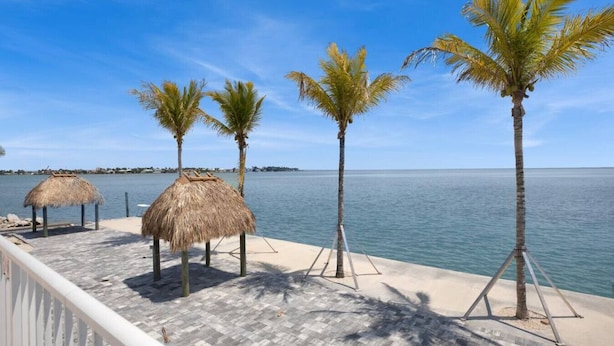 A beachside deck with thatched umbrellas and palm trees, overlooking calm waters. - Blue Octopus Hideaway at OI! (Marathon)