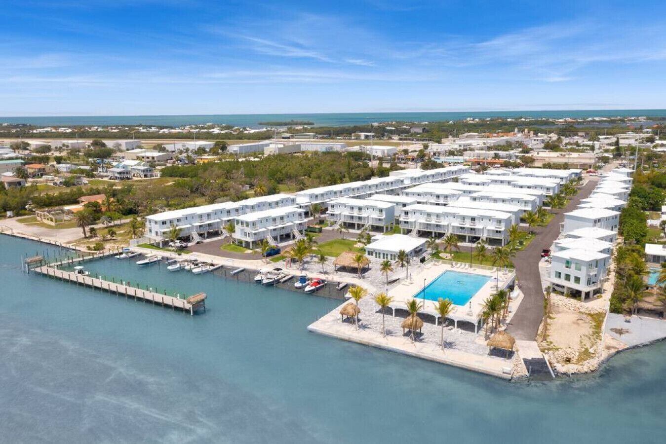 Een resort met meerdere witte gebouwen, een steiger met boten, een zwembad en een jachthaven.