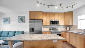 A modern kitchen with wooden cabinets, stainless steel appliances, a granite countertop, and a dining area with a blue sofa.