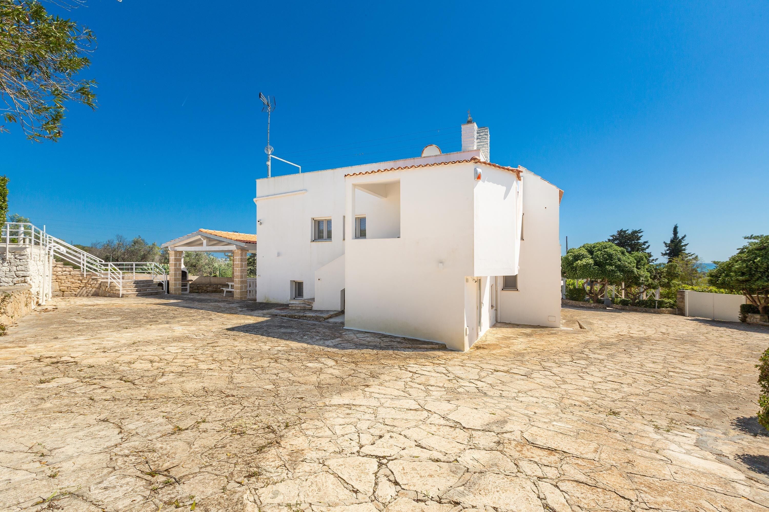 A white building with a tiled roof, a stone courtyard, and a staircase leading to a covered area.
