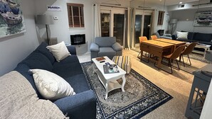 A living room with a sofa, armchair, coffee table, and a dining table with chairs. There is a TV mounted on the wall and a window with blinds. - Cozy WATERFRONT condo in a quiet cove.   Private Boat launch (Moneta)