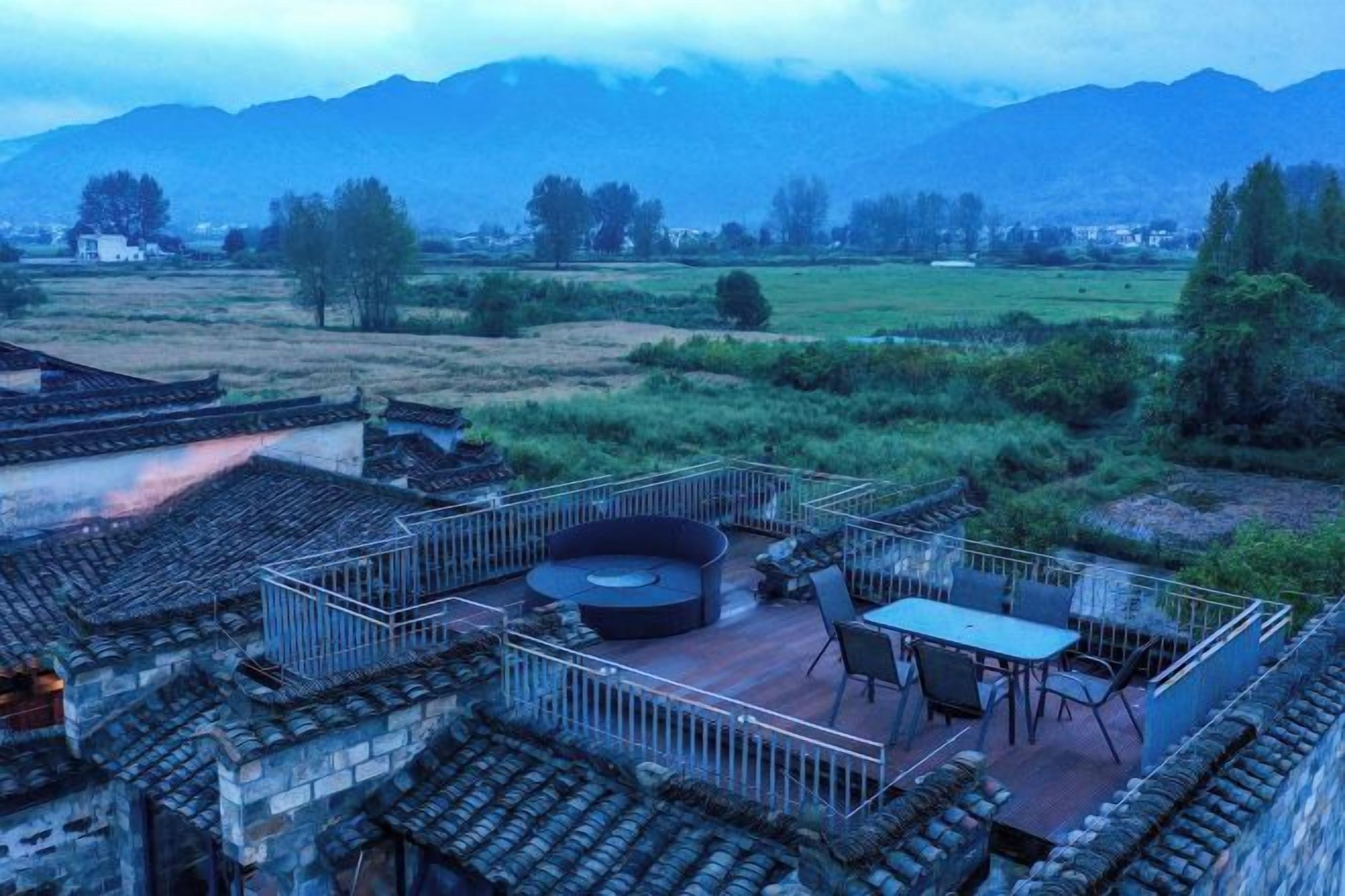 A traditional courtyard with a dining area, surrounded by stone walls and a view of distant mountains.