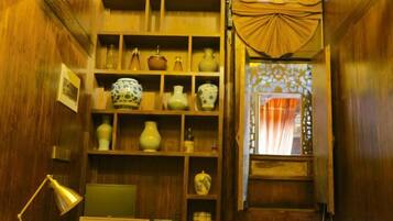 A room with wooden walls, shelves with decorative items, a desk with a lamp, and a window with curtains.