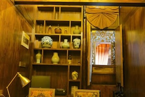 Una habitación con paredes de madera, estantes con adornos, un escritorio con lámpara y una ventana con cortinas.