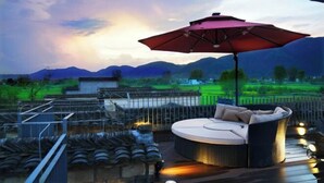 A rooftop terrace with a round outdoor sofa and a large umbrella, overlooking a mountainous landscape. - Ruiqi Xiangyun Inn (Yi County)