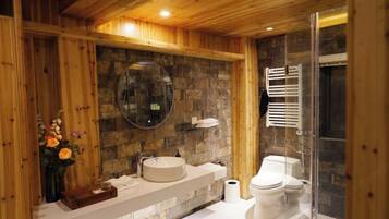Un bagno con parete in pietra, soffitto in legno, uno specchio rotondo, un lavandino, un WC e un box doccia in vetro.