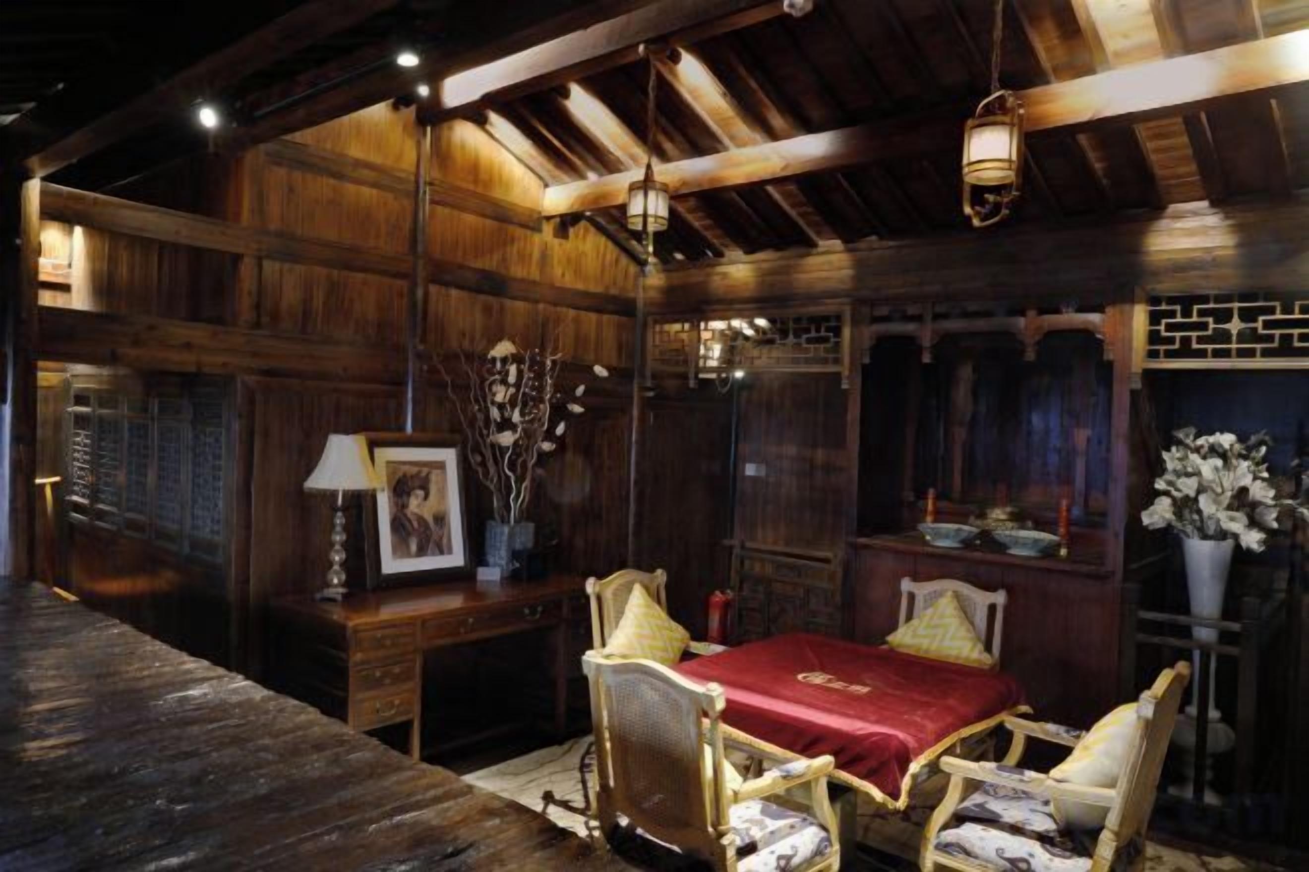A wooden room with a dining table, chairs, a lamp, and a vase with flowers.