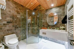 Et badeværelse med et brusebad bag glas, et hvidt toilet, en hvid vask og et spejl på væggen.