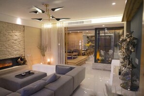 Een moderne woonkamer met een open haard, een bank en een eethoek, afgescheiden door een glazen wand.