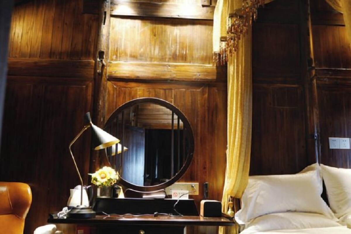 A wooden room with a bed, a desk with a lamp, and a mirror.