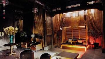 A traditional interior with a wooden floor, a seating area with cushions, and a window with curtains.