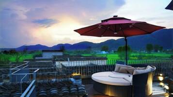 A rooftop terrace with a round seating area, a large umbrella, and a view of a green landscape.