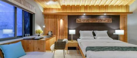 Une chambre d’hôtel moderne avec des panneaux de bois, un grand lit, des tables de chevet avec des lampes, un bureau et une fenêtre donnant sur un beau paysage.