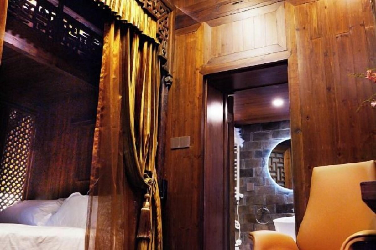 A wooden room with a bed, a chair, and a stone wall.