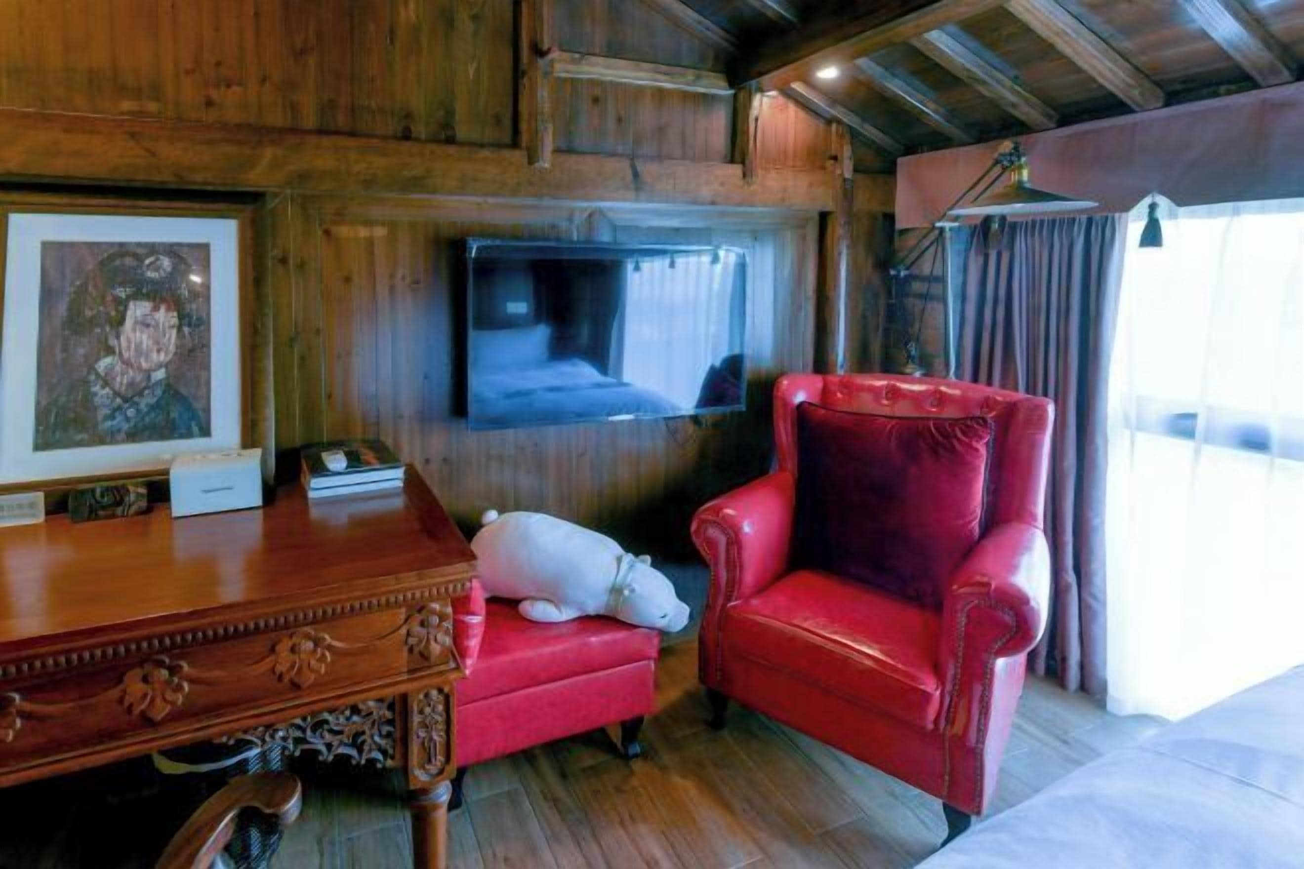 Un interior de madera con una silla de cuero rojo, una mesita y un televisor montado en la pared.