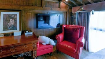 Un interior de madera con una silla de cuero rojo, una mesita y un televisor montado en la pared.