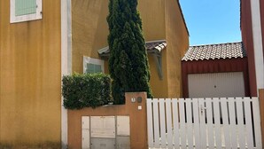 A yellow building with a white gate, a small window, and a tall green hedge.