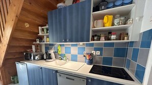 A compact kitchen with blue cabinets, a white countertop, a built-in dishwasher, and a stove.