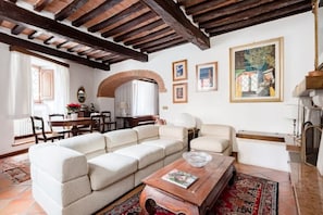 Una sala de estar con un sofá modular, una mesa de centro y una chimenea. Hay cuadros enmarcados en la pared y un comedor al fondo.