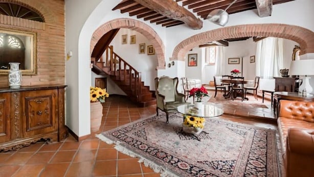 Un vaste espace de vie agrémenté d’un escalier en bois, d’un coin repas et d’une grande porte en arc de cercle.