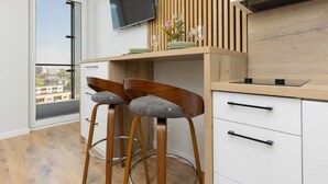 A modern kitchen with two bar stools, a flat-screen TV, and a view of the city through a large window.