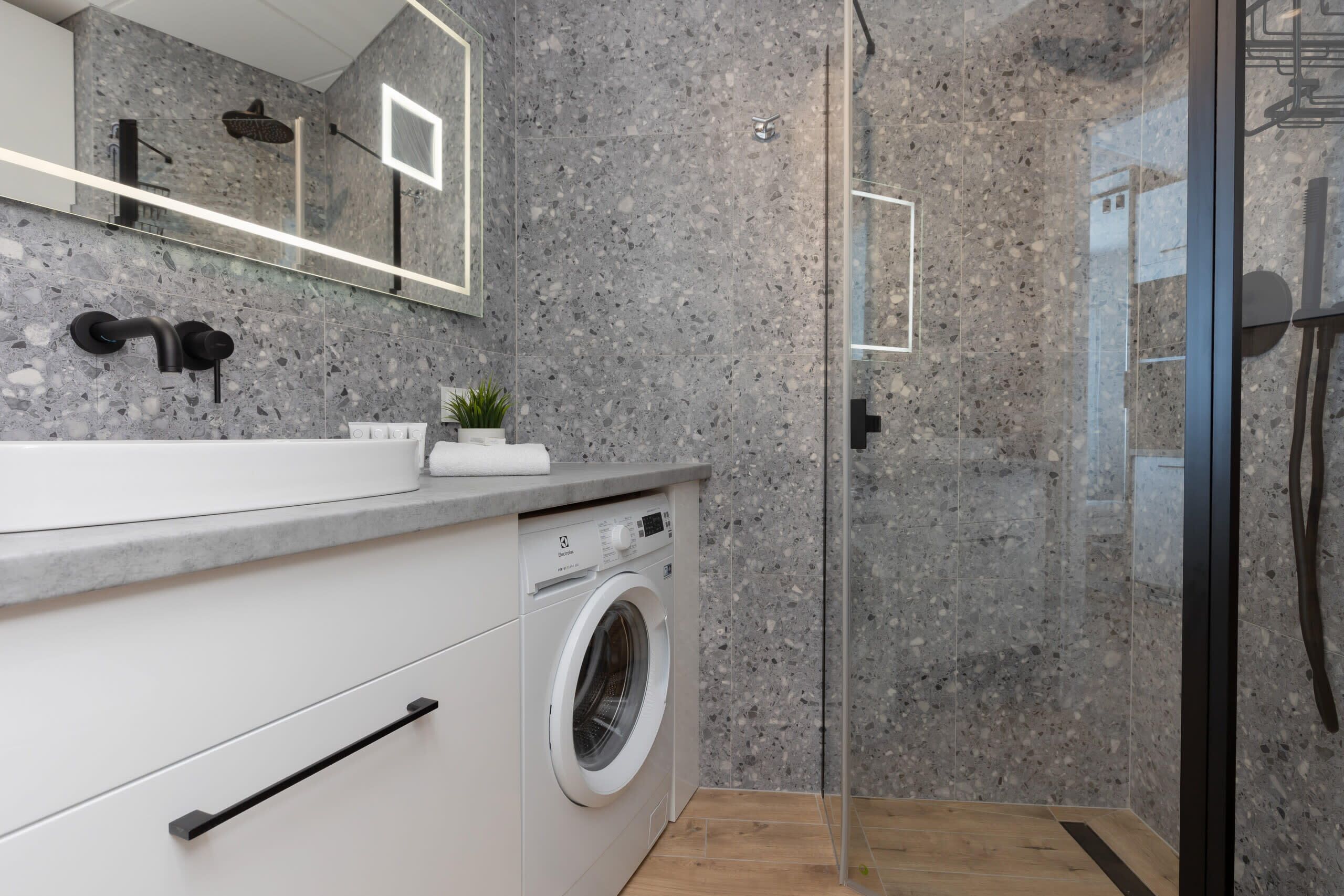 Un baño moderno con lavadora, cabina de ducha de vidrio y encimera de granito.