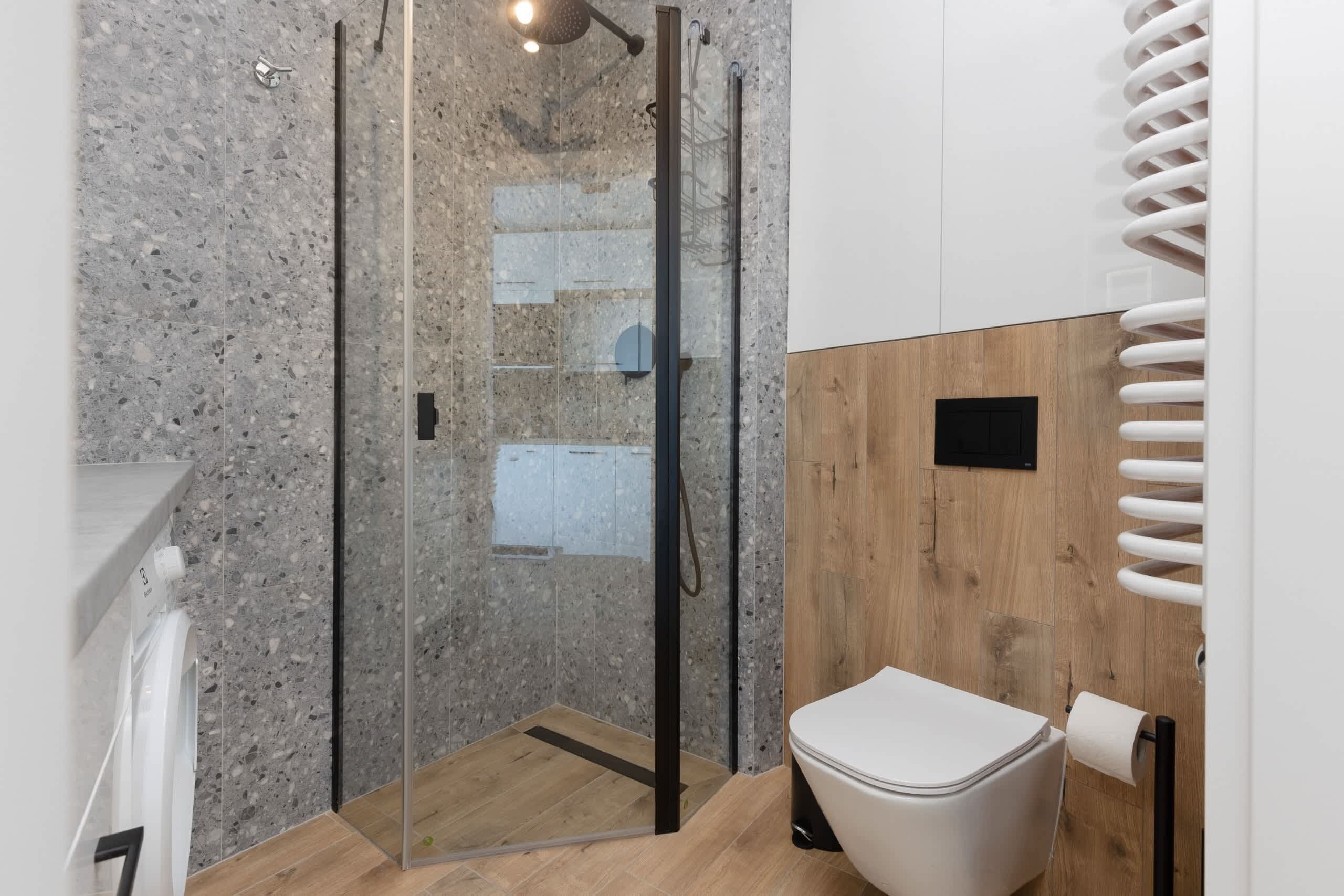A modern bathroom with a glass-enclosed shower, a white toilet, and a wooden panel wall.
