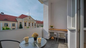 A balcony with a round table, two chairs, a potted plant, and a window overlooking a building with a red roof. - Stylish Apartment in Wroclaw | Balcony and Workspace (Wrocław)