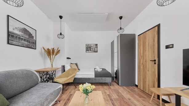 A modern room with a sofa, a small table with a vase, a bed, and a wooden door. - Stylish Apartment in Wroclaw | Balcony and Workspace (Wrocław)