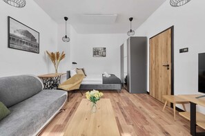 Una habitación moderna con sofá, una mesita de noche con un florero, cama y puerta de madera.