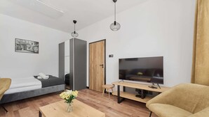 A modern living room with a sofa, a coffee table with flowers, a TV, and a wooden door. - Stylish Apartment in Wroclaw | Balcony and Workspace (Wrocław)