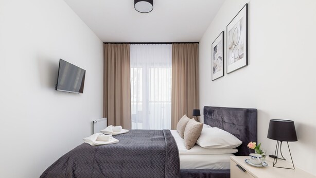A modern hotel room with a bed, bedside table, lamp, and artwork on the wall. - Stylish Apartment | 500 m to the Beach, Parking, Balcony (Grzybowo)
