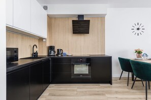 A modern kitchen with black cabinetry, a built-in oven, a coffee maker, and a clock on the wall.