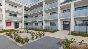 A multi-story building with balconies, a paved courtyard, and a small garden area. - Stylish Apartment | 500 m to the Beach, Parking, Balcony (Grzybowo)