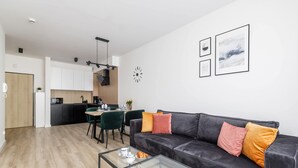 A modern living room with a leather sofa, a glass coffee table, and a dining area with a green chair and a small table. - Stylish Apartment | 500 m to the Beach, Parking, Balcony (Grzybowo)