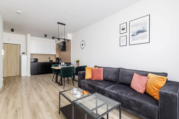 A modern living room with a leather sofa, a glass coffee table, and a dining area with a green chair and a small table.