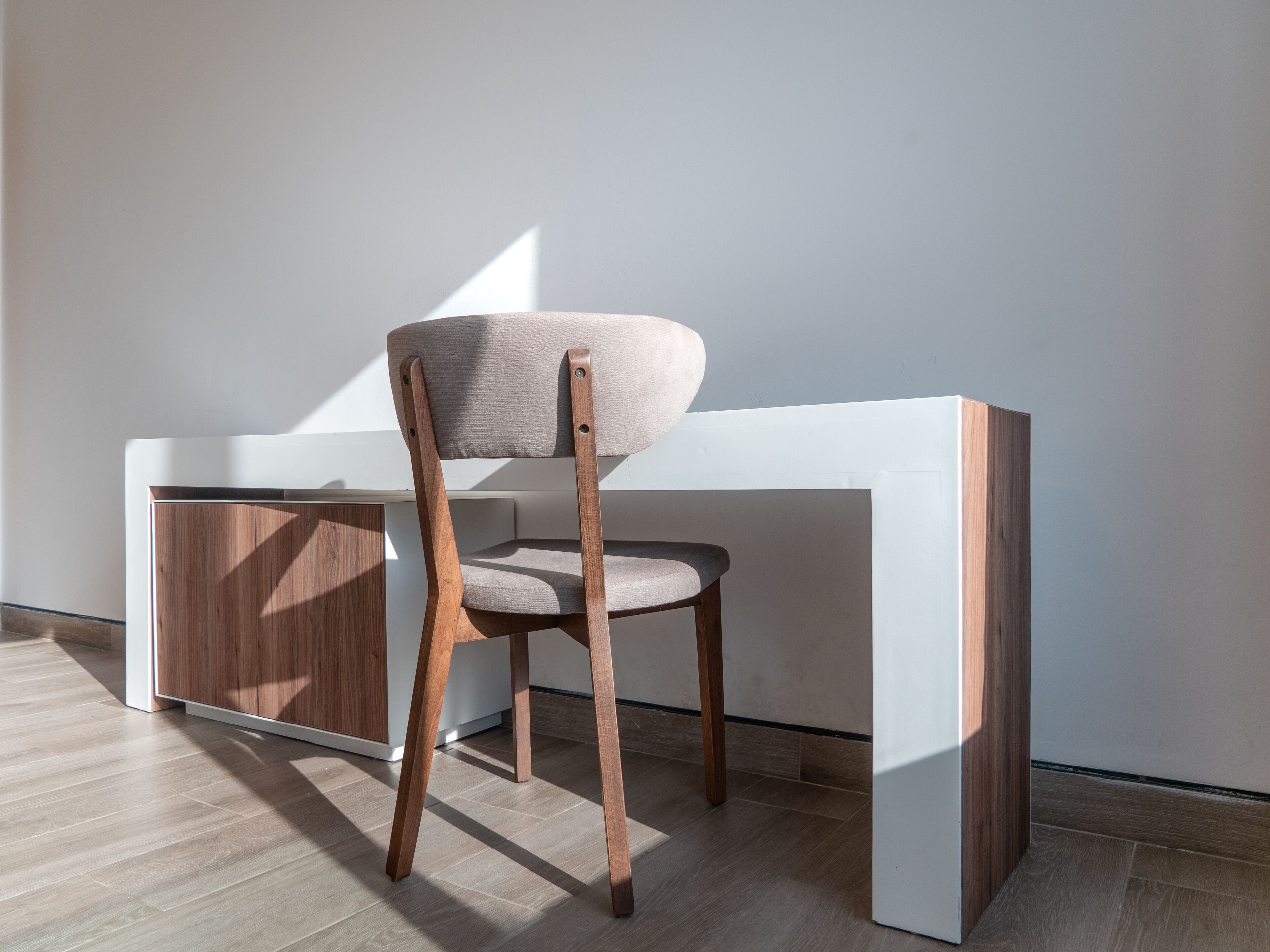 A modern chair with a wooden frame and fabric seat, positioned next to a white desk with a wooden side panel.