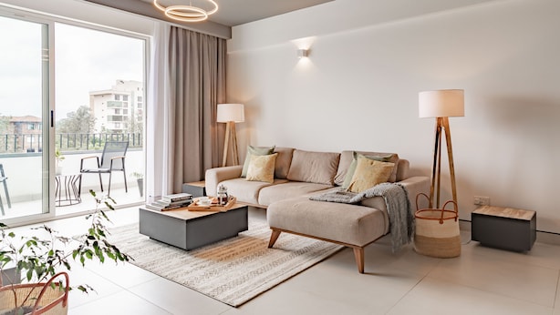 A modern living room with a sofa, coffee table, and floor lamp. There is a large window with curtains, a plant, and a view of buildings outside. - Purple Haze by Aircasa (Nairobi)